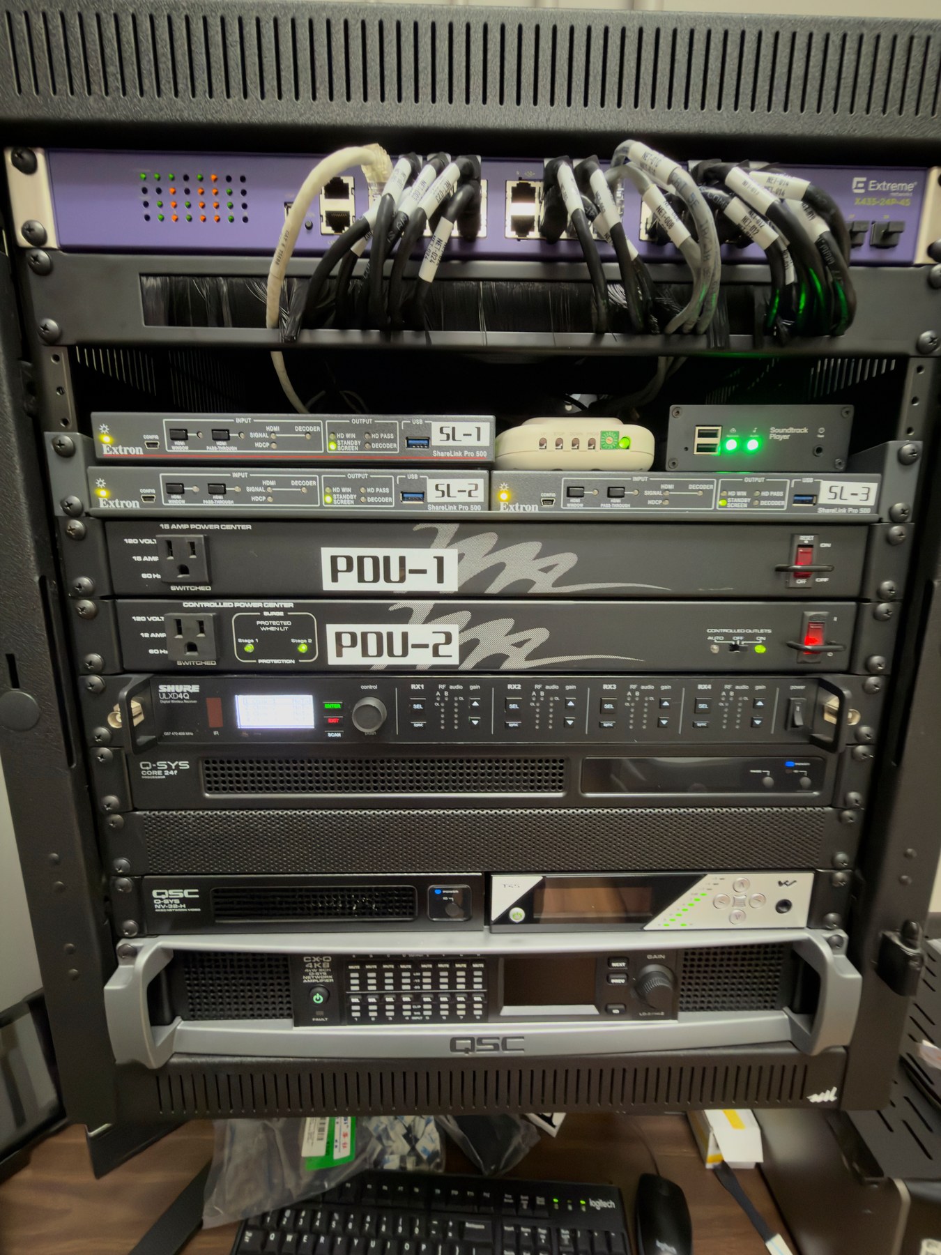 Completed Classic Room Q-SYS equipment rack with labeled network, video, collaboration, microphone, processing, and amplifier hardware